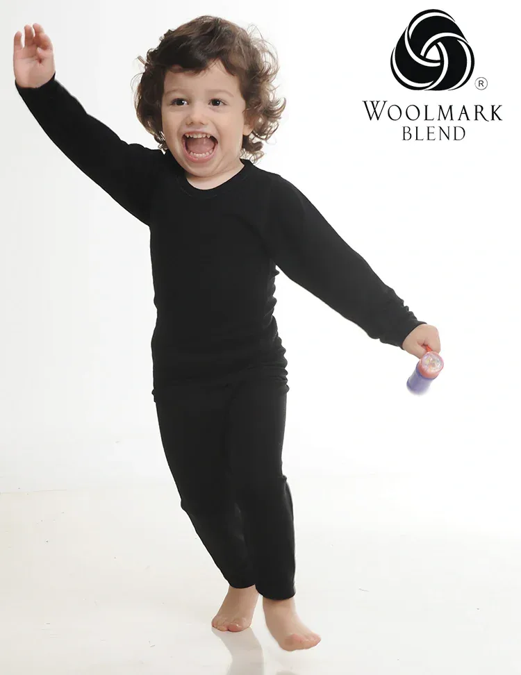 550SS%20-%20Children%27s%20Black%20Wool%20Long%20Sleeve%20Shirt%20-%20550SS Bright happy child dancing in black pajamas with Woolmark Blend logo in studio setting.