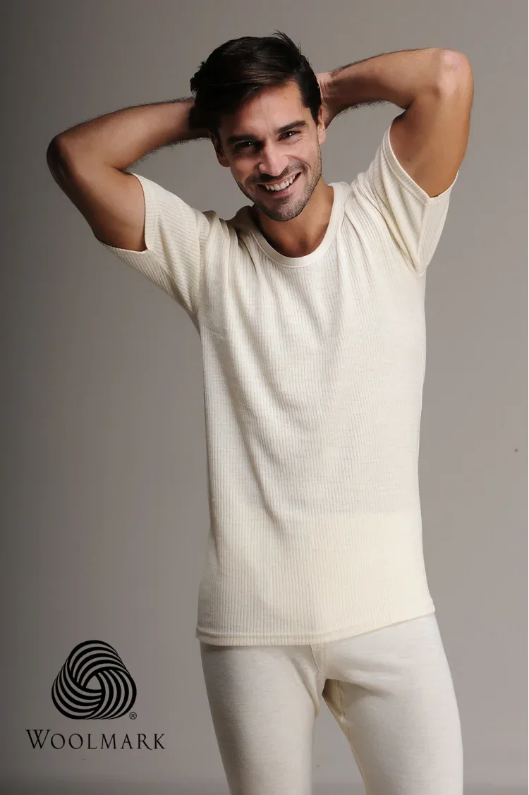 1000%20-%20Men%27s%20100%25%20Wool%20Short%20Sleeve%20Undershirt%20-%201000 Soft cream ribbed t-shirt worn by smiling man with hands behind head, casual look, Woolmark logo, minimal background, emphasizing comfort and quality.