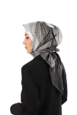 Elegant woman wearing a stylish silk hijab with black, white, and grey abstract patterns, paired with a black blazer, showcasing Middle Eastern fashion and cultural accessories.