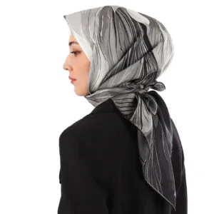 Elegant woman wearing a stylish silk hijab with black, white, and grey abstract patterns, paired with a black blazer, showcasing Middle Eastern fashion and cultural accessories.
