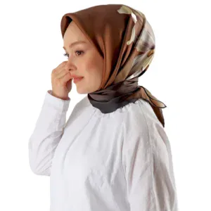 Elegant woman wearing a silky, patterned hijab in shades of brown, beige, and cream, paired with a white top, showcasing modest fashion and Turkish heritage styles.