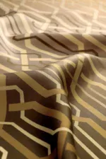 Intricate geometric patterned fabric in beige and brown tones, showcasing detailed design and smooth texture for stylish home decor or fashion accessories.