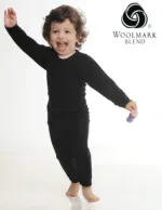 Bright happy child dancing in black pajamas with Woolmark Blend logo in studio setting.