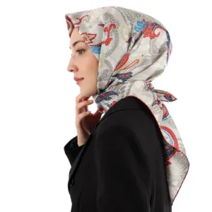 Elegant woman wearing a patterned silk hijab in red, blue, and gray tones, paired with a classic black blazer, showcasing stylish modest fashion from Turkey with a focus on quality and fast shipping.