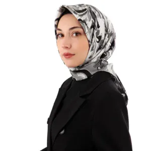 Elegant woman wearing a stylish black blazer and a silk floral hijab, showcasing modern modest fashion with a clean white background.