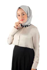 Elegant woman wearing a light gray hijab and beige blouse, smiling confidently, against a white background.