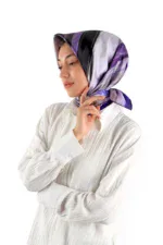 Elegant woman wearing a stylish purple and black silk headscarf, dressed in a white textured blouse, posing thoughtfully against a plain white background.