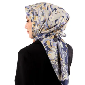 Elegant floral-patterned silk hijab with soft pastel shades of blue, beige, and cream, styled on a woman wearing a black outfit, suitable for fashionable modest wear.