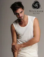 Smooth-skinned man in white sleeveless tank top posing against grey background with Woolmark Blend logo | fashionable men's casual wear on Shop of Turkey website.