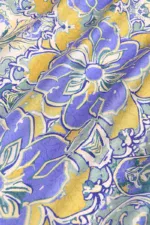 Vibrant floral patterned fabric featuring purple, yellow, and green hues, perfect for fashion and home decor projects.