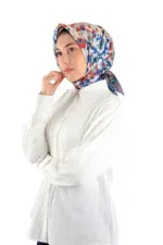 Vibrant floral-patterned silk headscarf with red, blue, and beige tones, styled with a white button-up shirt on a model posing in a studio environment.