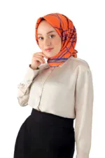 Vibrant orange and blue patterned silk scarf styled as hijab worn by a young woman in a beige blouse and black skirt on a white background.