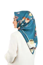 Vibrant floral silk hijab in shades of blue, peach, and cream, styled on a woman with a white blazer for elegant and modest fashion.