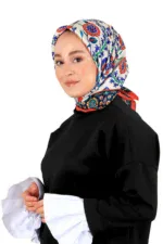 Elegant woman wearing colorful patterned headscarf and black traditional dress with white sleeves, smiling confidently on a white background.