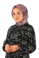 Elegant woman wearing a silky lavender hijab and a black dress with white abstract floral patterns, standing confidently for a fashion photoshoot.