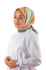 Colorful patterned silk hijab with peach, green, and brown tones worn by a woman with fair skin, brown eyes, and natural makeup on a plain white background.