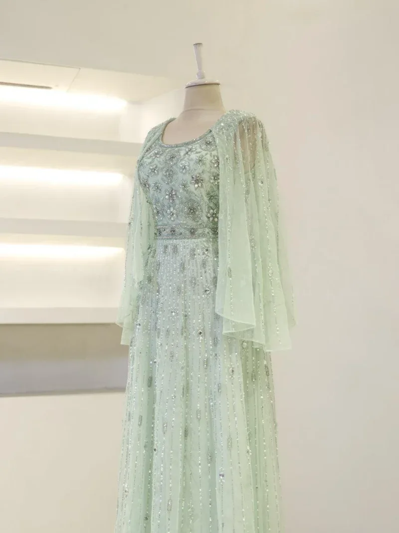 Luxurious pale green embroidered gown with intricate beadwork and sheer cape details, perfect for special occasions and events.