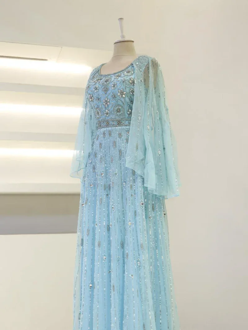 Elegant turquoise dress with intricate silver embroidery, beading, and layered chiffon sleeves, perfect for special occasions or traditional celebrations.