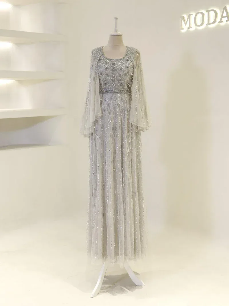 A stunning silver and white embellished gown with intricate beadwork and flowing sheer cape for weddings or special occasions. Features detailed embroidery, long length, and luxurious fabric.