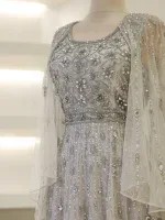 Luxurious white dress with intricate bead and sequin embroidery, featuring floral motifs on the bodice, sheer sleeves, and flowy fabric for a sophisticated look.