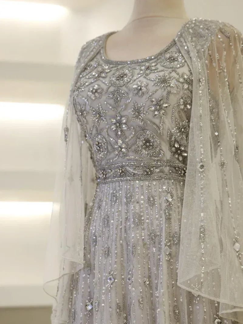 Luxurious white dress with intricate bead and sequin embroidery, featuring floral motifs on the bodice, sheer sleeves, and flowy fabric for a sophisticated look.