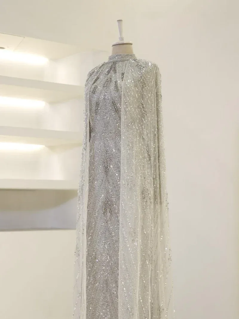 Elegant white gown with intricate beadwork and sequins, perfect for weddings or special occasions. Folded cape adds a regal touch to this stunning dress.