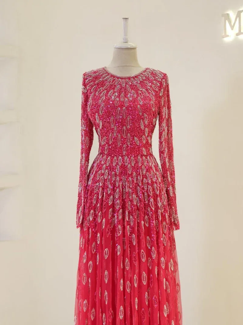 Stunning pink evening gown featuring intricate embroidery and sequins, long sleeves, and a flowing skirt perfect for formal occasions or special events.