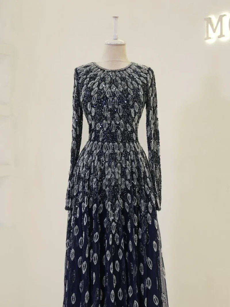Luxurious black evening dress decorated with intricate silver embroidery and sequins, featuring a long fitted silhouette with sheer long sleeves and a flowing skirt, perfect for formal occasions.