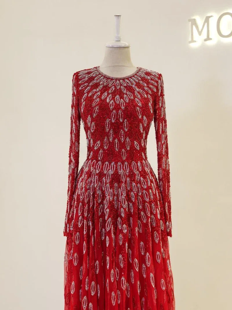 Gorgeous red evening gown with intricate silver beadwork, long sleeves, and a flowing skirt perfect for special occasions and formal events.