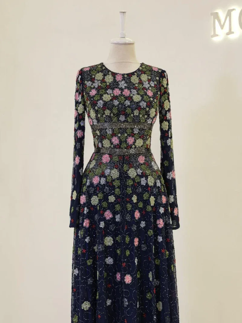 Stylish long-sleeve dress with intricate floral embroidery in pink, green, and white on a dark navy background, perfect for special occasions or upscale events.