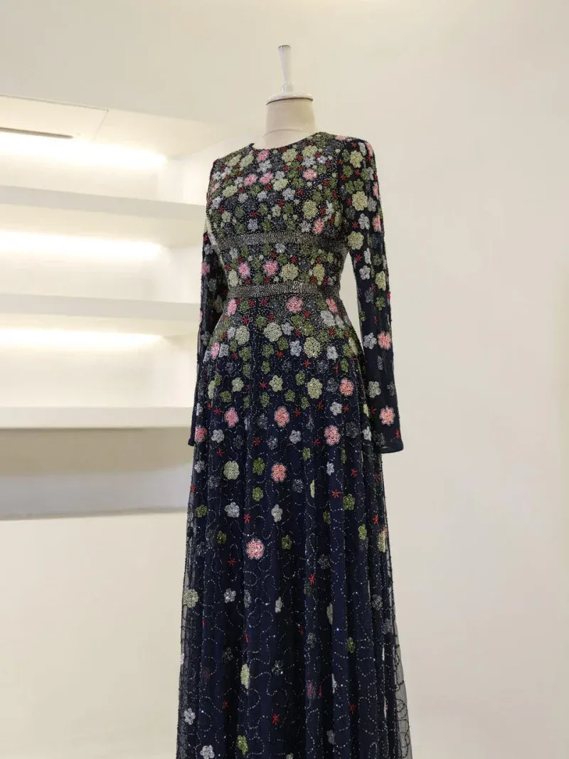 A stunning long dress with intricate floral embroidery in pink, green, and white on a navy blue background. Features long sleeves and a fitted waist, perfect for formal occasions.