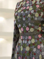 Intricate beaded floral embroidery with pink, green, gray, and red accents on black fabric, showcasing craftsmanship and vibrant detail.