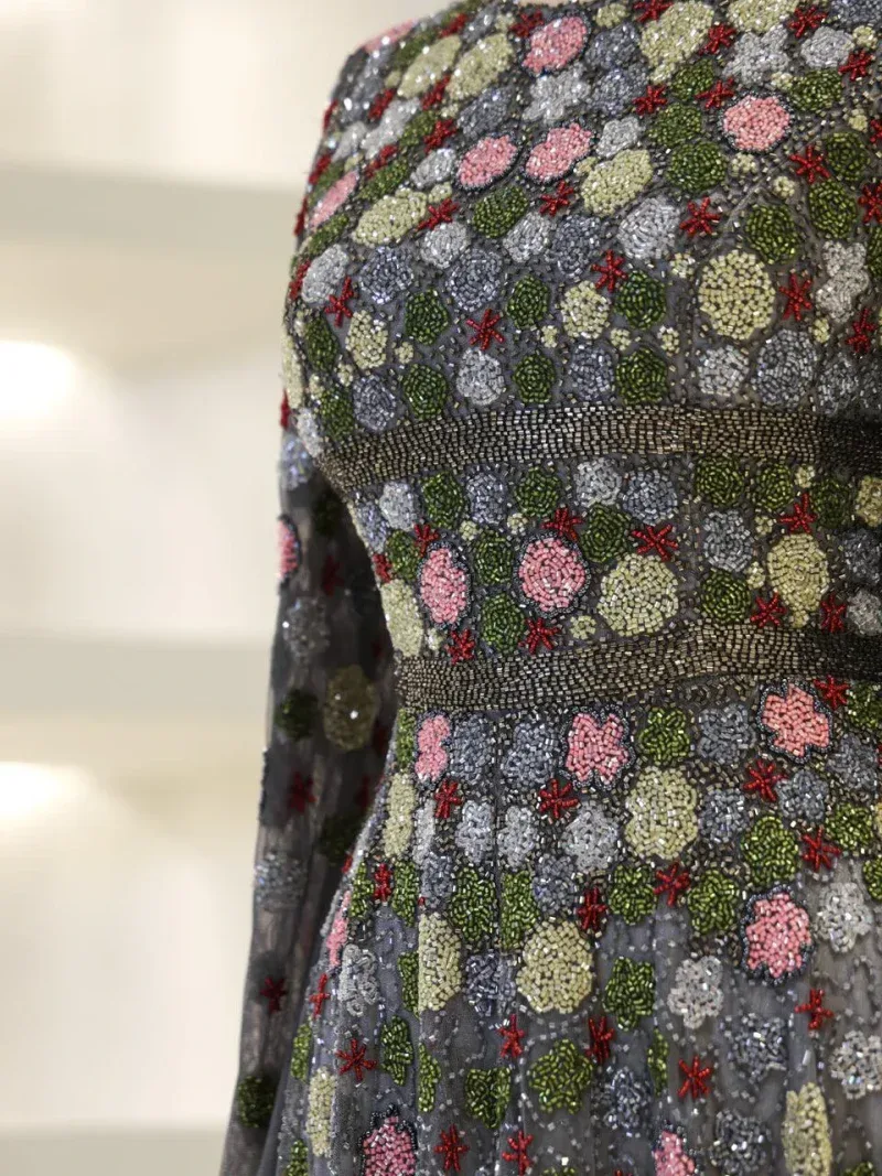 Intricate beaded floral embroidery with pink, green, gray, and red accents on black fabric, showcasing craftsmanship and vibrant detail.