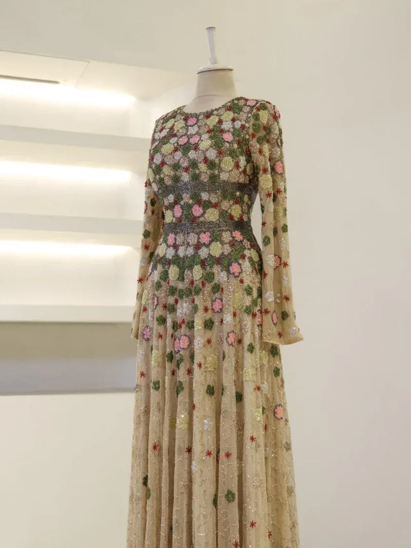 Luxurious long dress with intricate floral embroidery in pink, green, red, and gold on sheer fabric, perfect for special occasions or evening events.