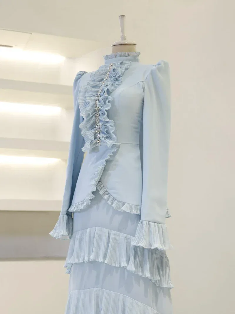 Stylish light blue dress featuring ruffled details, layered pleats, and pearl accents perfect for special occasions or fashion-forward events.