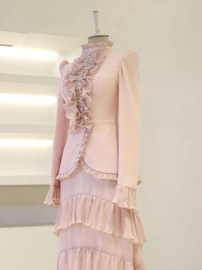 A stylish pink dress featuring ruffled accents, pearl embellishments, and layered pleats, perfect for fashion-forward occasions and formal events.