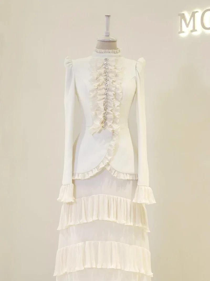 Stunning white dress featuring ruffled front detailing and pearl-like embellishments, with pleated layered skirt and puffed shoulders, perfect for formal or special occasions.