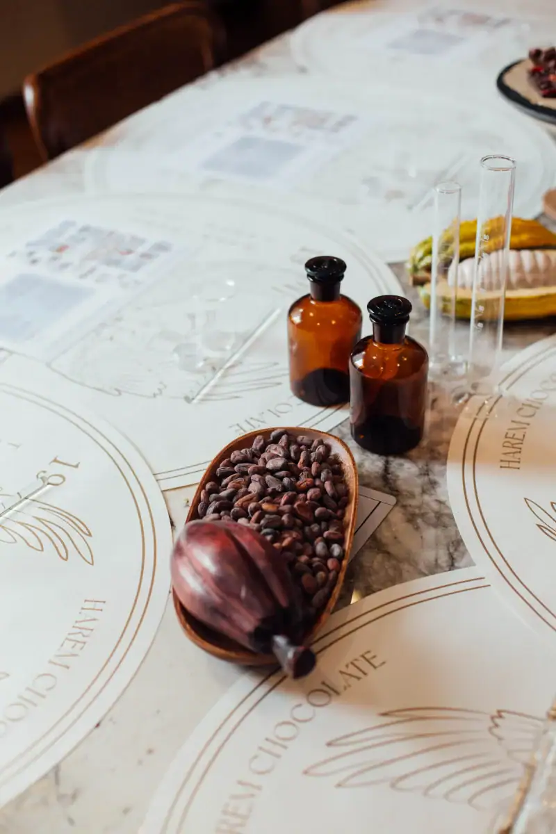 1. Laboratory glassware, cocoa beans, and vintage bottles on a marble table, with menus in the background for a Turkish specialty chocolate tasting experience.