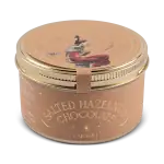 Cream-colored metal tin with artistic illustration of a woman reading, labeled "Salted Hazelnut Chocolate - Caramel" from Shop of Turkey, emphasizing authentic Turkish sweets with fast shipping.