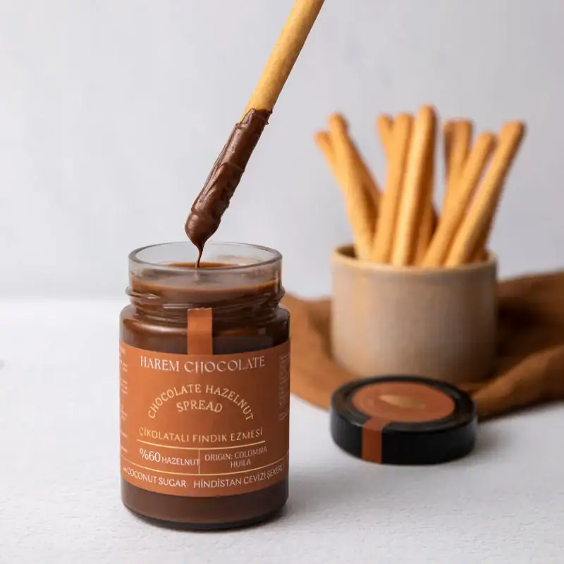 Rich chocolate hazelnut spread with a biscuit stick dipped in chocolate, on a white surface with a container of crispy breadsticks in the background.