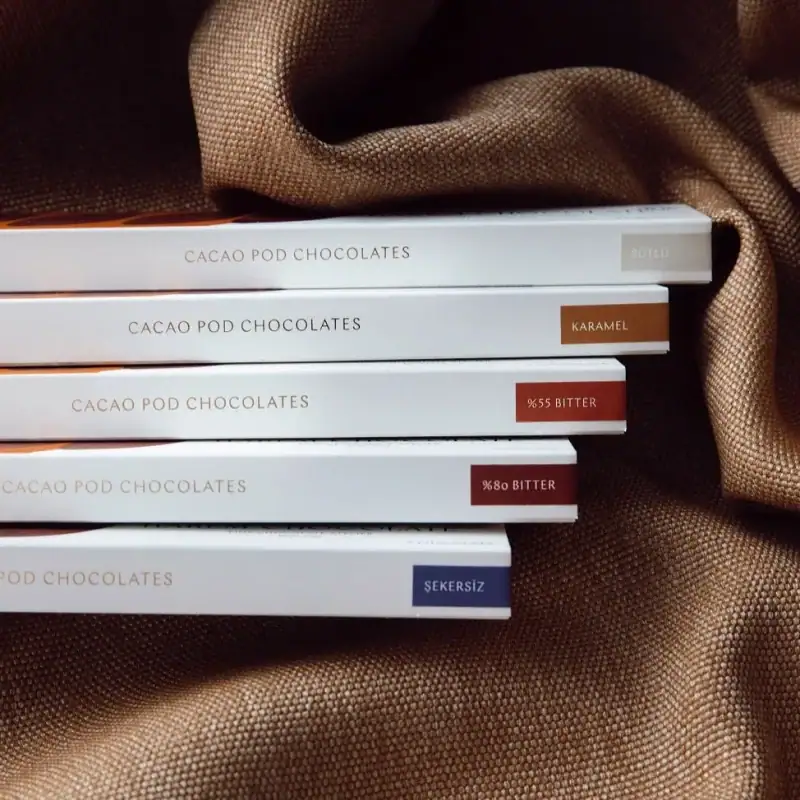 1. Assorted cacao pod chocolates with flavors including caramel, bitter, and unsweetened, displayed on a silky fabric background for a premium Turkish confectionery experience.