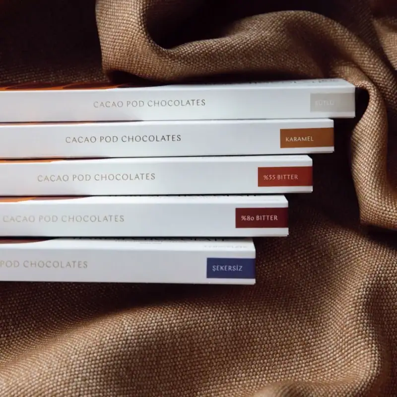 Delicious Turkish cacao pod chocolates in various flavors, including bitter, caramel, and unsweetened, displayed on a textured brown fabric for premium gift options.