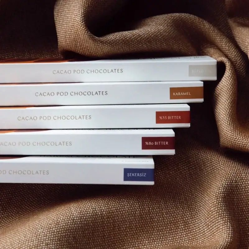 Rich, dark chocolate cacao pod chocolates with various flavors including caramel, bitter, and sugar-free options, beautifully packaged on a textured brown fabric background.