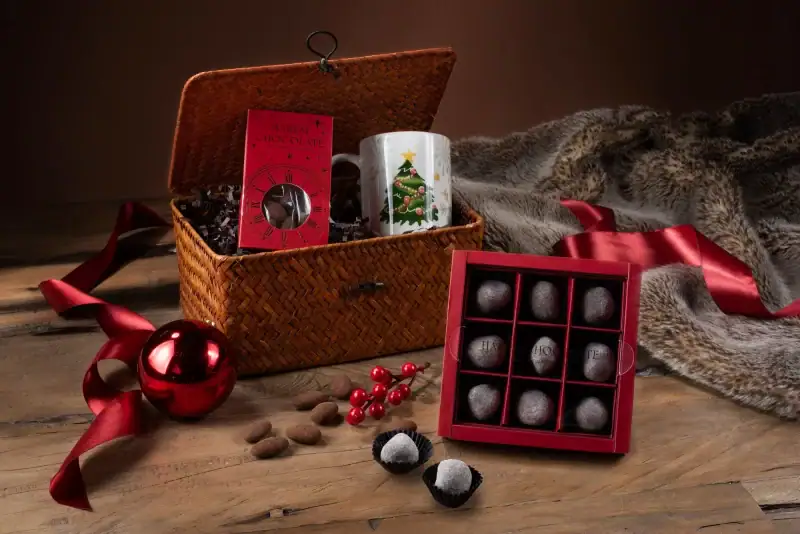 Deluxe Turkish chocolates and Christmas-themed gifts in a woven basket, perfect for holiday celebrations, with festive decorations and a cozy fur blanket on a rustic wooden surface.
