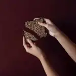 Richly textured chocolate bars with chopped nuts on top, held by a person's hands against a dark background.