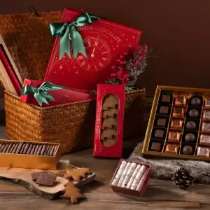 Assorted Turkish chocolates and confectionery gifts in festive packaging with pinecones and holiday decor on a wooden surface.