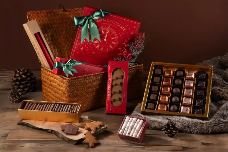 Assorted Turkish chocolates and confectionery gifts in festive packaging with pinecones and holiday decor on a wooden surface.