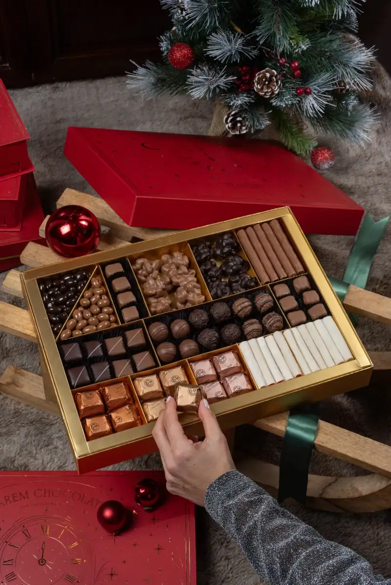 1. Luxurious box of assorted chocolates and candies set against a festive Christmas background with a decorated tree.
