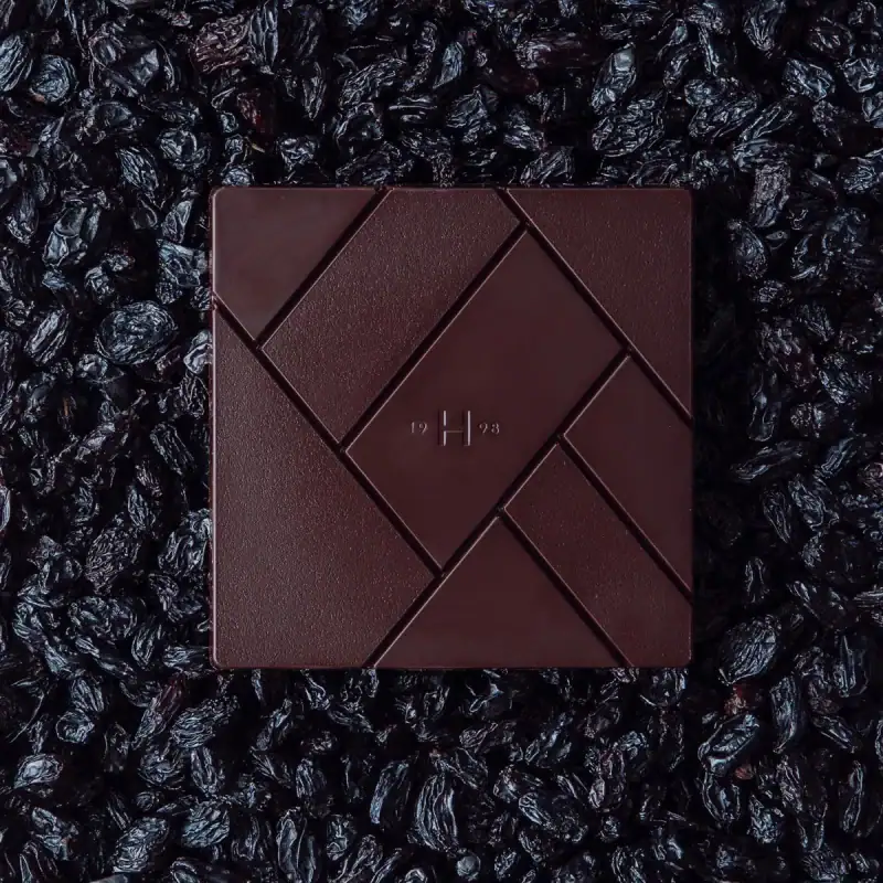 Dark chocolate palette with geometric design and embossed “H” on surface, surrounded by dried black mulberries, ideal for gourmet, gift, or luxury packaging.