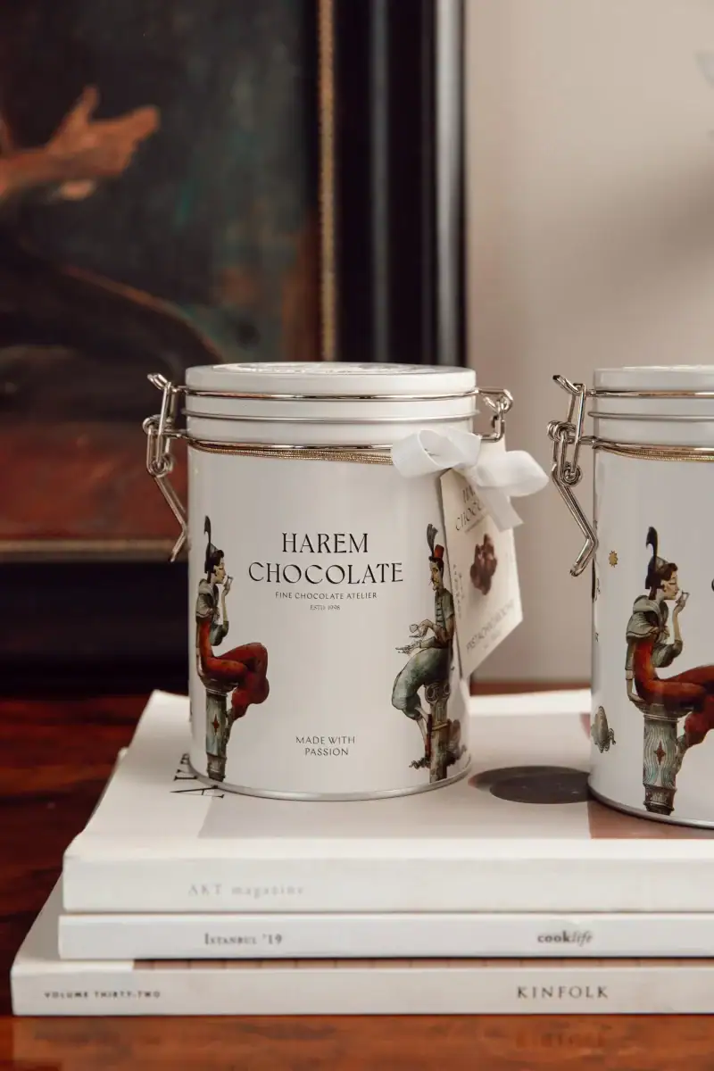 Vintage-style metal tins of Harem Chocolate with artistic illustrations, placed on top of a stack of magazines for sale from Turkey with fast worldwide shipping.